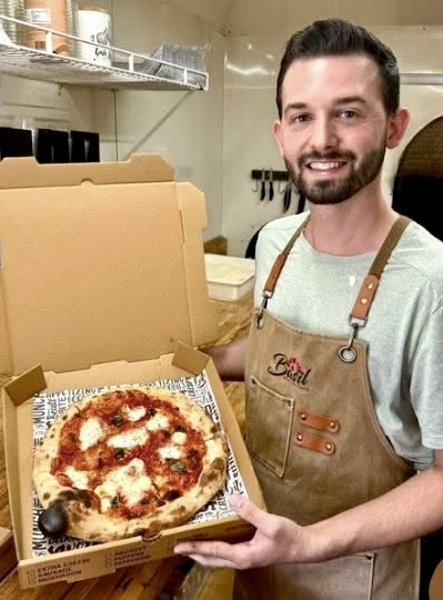 Owner Wesley Sumner holding a fresh wood-fired Margherita pizza